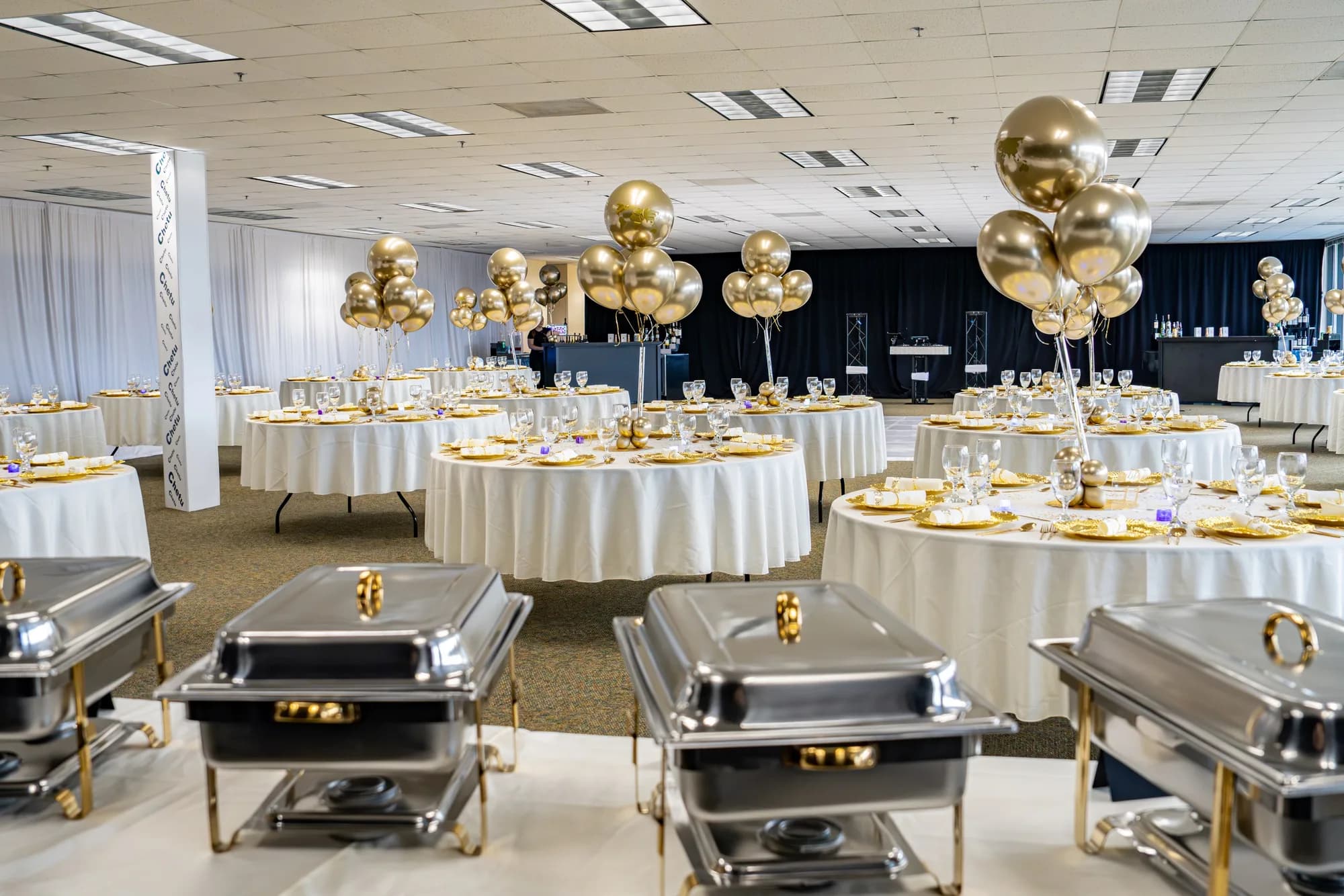 Ballroom set with gold balloons and a catered buffet for a corporate celebration