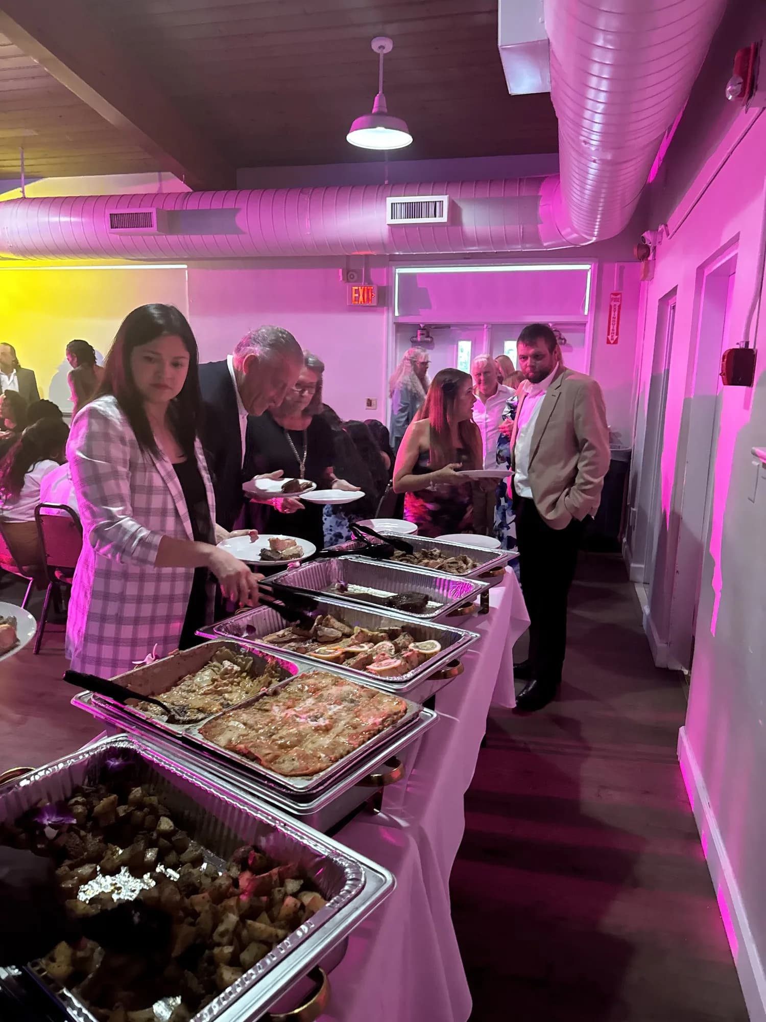 Guests at a buffet under pink uplighting at a catered party