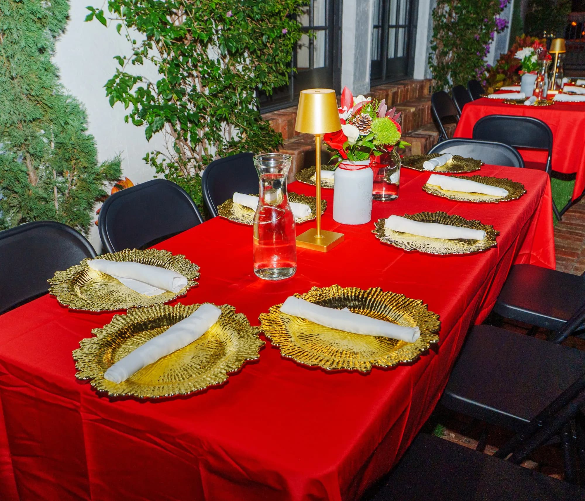 Red linen table with gold chargers at an outdoor dinner